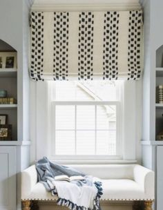 a white bench sitting under a window next to a book shelf with books on it