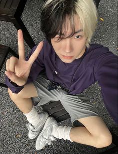 a young man with white hair giving the peace sign while sitting on a wooden bench