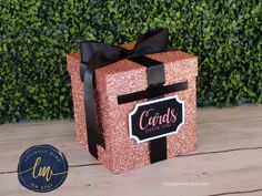 a pink gift box with a black ribbon and name card on it sitting on a wooden table