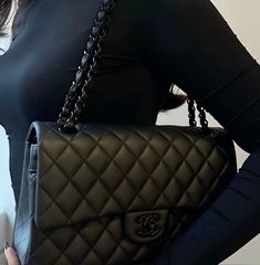 a woman is holding a black chanel bag