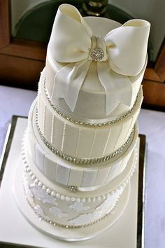 a three tiered white wedding cake with pearls and bows