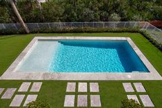 an aerial view of a swimming pool in the middle of a grassy area with stepping stones