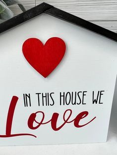 a sign that says in this house we love with a red heart on the front