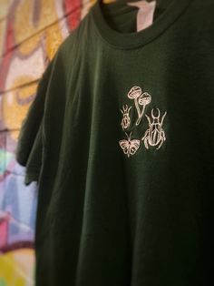 a green t - shirt with bugs on it hanging from a wall covered in graffiti