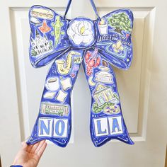 a hand is holding up a blue door bow with pictures on it that say no la