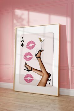 a framed photo with pink lipstick and high heeled shoes on the floor in front of a pink wall