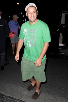 a man in a green shirt and hat is walking down the street with his hands in his pockets