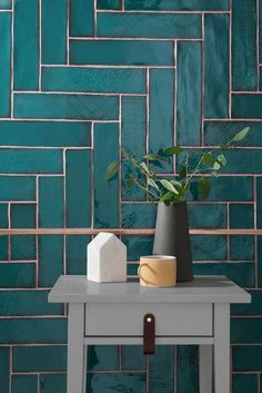 a white table with a vase on top of it next to a green brick wall