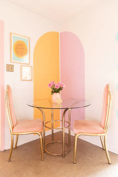 a glass table with two chairs and a vase on it in front of a yellow wall