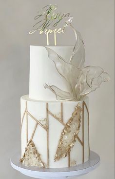 a white and gold wedding cake with flowers on the top is topped with an acrylic leaf