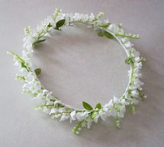 a white flower crown with green leaves and flowers on the headband is laying on a table