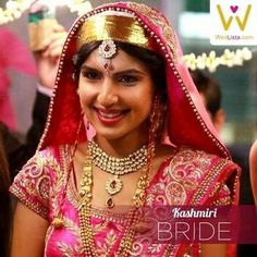 a woman in a pink and gold bridal outfit smiling at the camera with other people around her