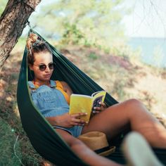 a woman sitting in a hammock reading a book