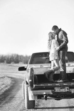 a man and woman kissing in the back of a pick up truck on a dirt road