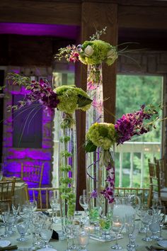 tall vases filled with flowers and greenery sit on top of a round table