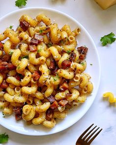 a white plate topped with pasta covered in bacon and parsley next to a fork