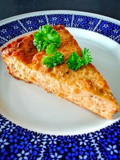 a slice of quiche on a blue and white plate with parsley garnish