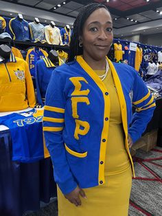 a woman standing in front of a display of sports jerseys at a sporting event, wearing a blue and yellow jacket with the word spirit written on it