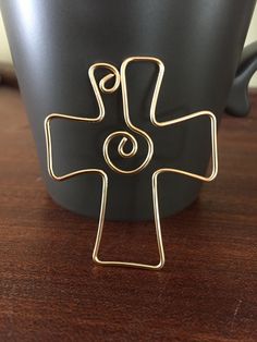 a gold cross brooch sitting on top of a table next to a black cup