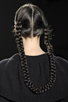 a woman with two braids in her hair on the catwalk, looking down