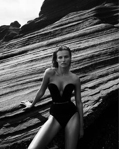 a black and white photo of a woman in a bathing suit sitting on the beach