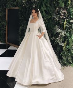 a woman standing in front of a green wall wearing a white wedding dress and veil