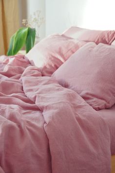 a bed with pink sheets and pillows on top of it, next to a plant