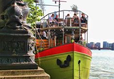 the boat is painted green, red and yellow with people sitting on it's deck