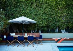 an outdoor table with chairs and umbrella next to a swimming pool