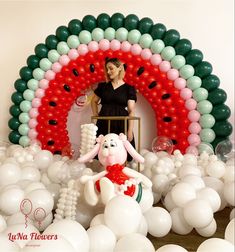 a woman standing in front of a balloon arch with balloons all around her and a stuffed bunny on the chair