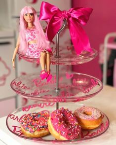 a barbie doll sitting on top of a three tiered tray filled with donuts