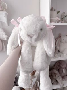 a person holding a white stuffed animal in their hand with other stuffed animals on the shelves behind them