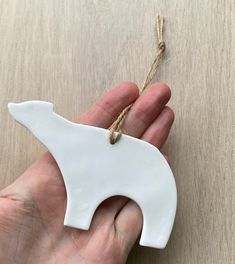 a hand holding a white ceramic bear ornament on a wooden table with twine