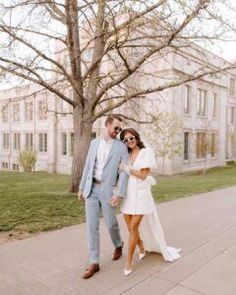 a man and woman are walking down the sidewalk in front of a large white building