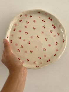 a hand holding a white plate with red flowers on it