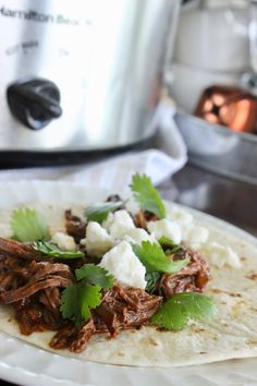 shredded meat and cilantro on a tortilla with an instant pressure cooker in the background