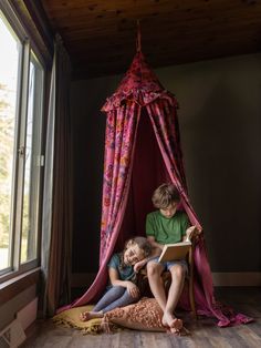 two children sitting on the floor in front of a pink canopy bed with drapes