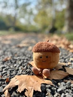 a stuffed acorn sitting on the ground next to leaves and a tree in the background