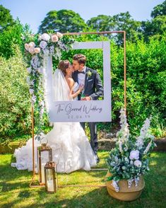 a bride and groom kissing in front of an outdoor wedding photo frame with flowers on it