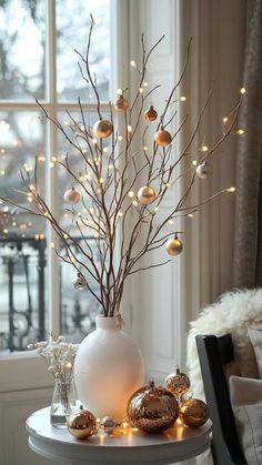 a white vase sitting on top of a table filled with christmas balls and branches in front of a window