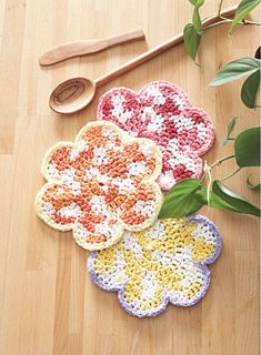 three crocheted flower coasters sitting on top of a wooden floor next to a plant