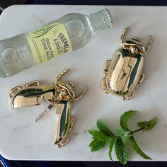 two gold - plated bugs on a marble table next to a bottle of water