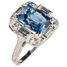 A dramatic cocktail ring in the Art Deco style centers on a cushion cut sapphire surrounded by four rectangular step-cut diamonds. Each corner is set with a full-cut melee and the shoulder shank is pavé-set with 98 full-cut melee. Accompanied by GIA report indicating a natural sapphire of Madagascar origin with no indication of heat. Size 7.5 Sapphire weighs approximately 6.39 carats Approximately 1.44 carats of diamonds 18k white gold Engagement Rings Romantic, Pink Opal Ring, Blue Sapphire Diamond Ring, Sapphire Cocktail Ring, Art Deco Brooch, Vintage Cocktail Ring, Gold Chanel, Sapphire And Diamond Ring, Blue Sapphire Diamond