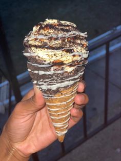 a hand holding an ice cream cone with chocolate and white icing on it, in front of a railing