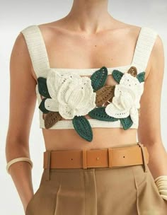 a woman wearing a crop top with crochet flowers on it's chest