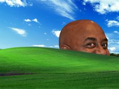 a man's head peeking over the top of a green hill with blue skies in the background