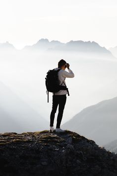 a person standing on top of a mountain with a backpack and binoculars in their hands