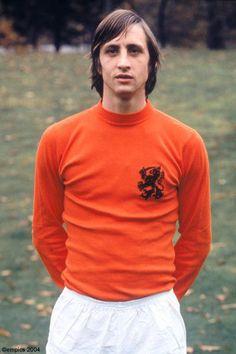 a young man in an orange shirt and white shorts standing in front of a field