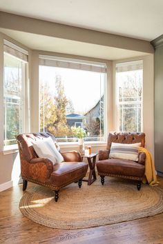 a living room with two leather chairs and a rug in front of the couches