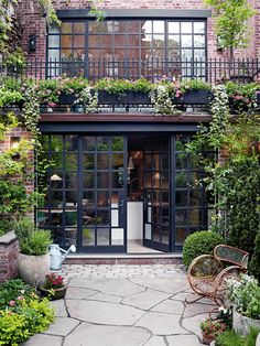 the front entrance to a brick building with lots of plants and flowers growing on it